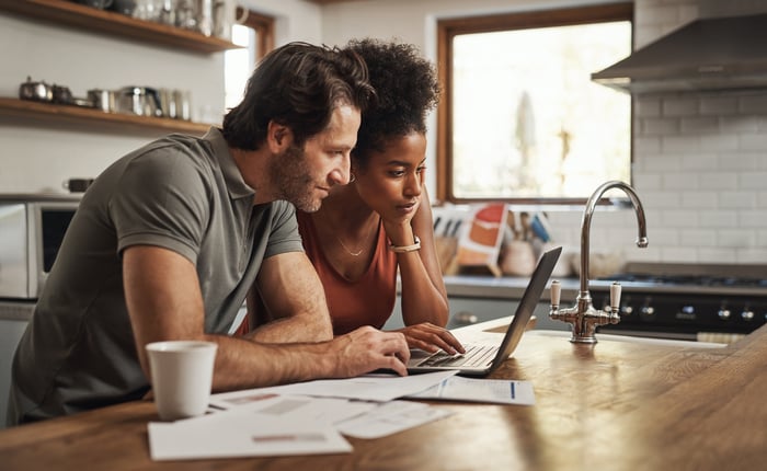 Couple researching on computer  in kitchen. 