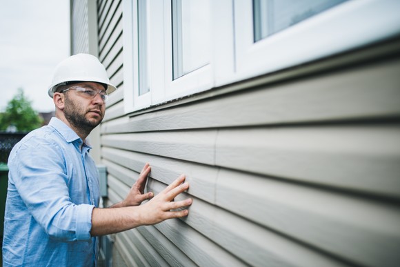 A worker examining new siding on a house. 