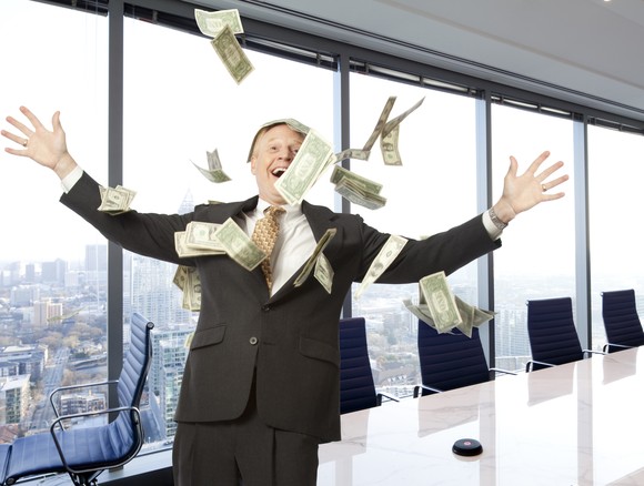 Happy person in a conference room, with arms spread wide and cash falling through the air.