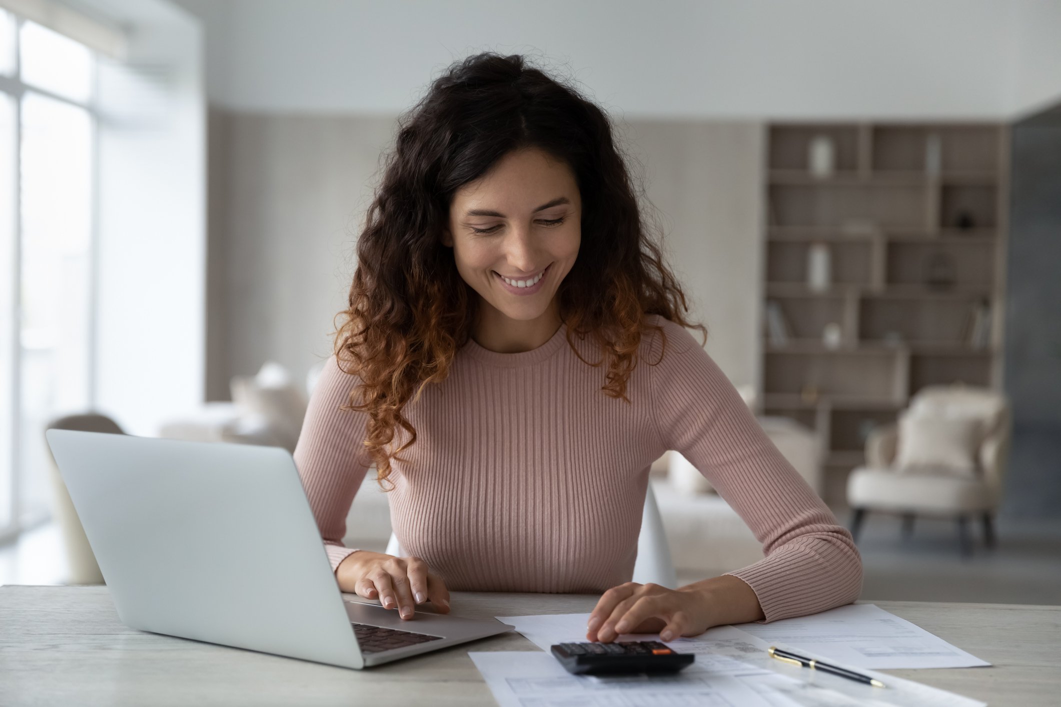 A person works on their finances on a desk with a laptop and  calculator.