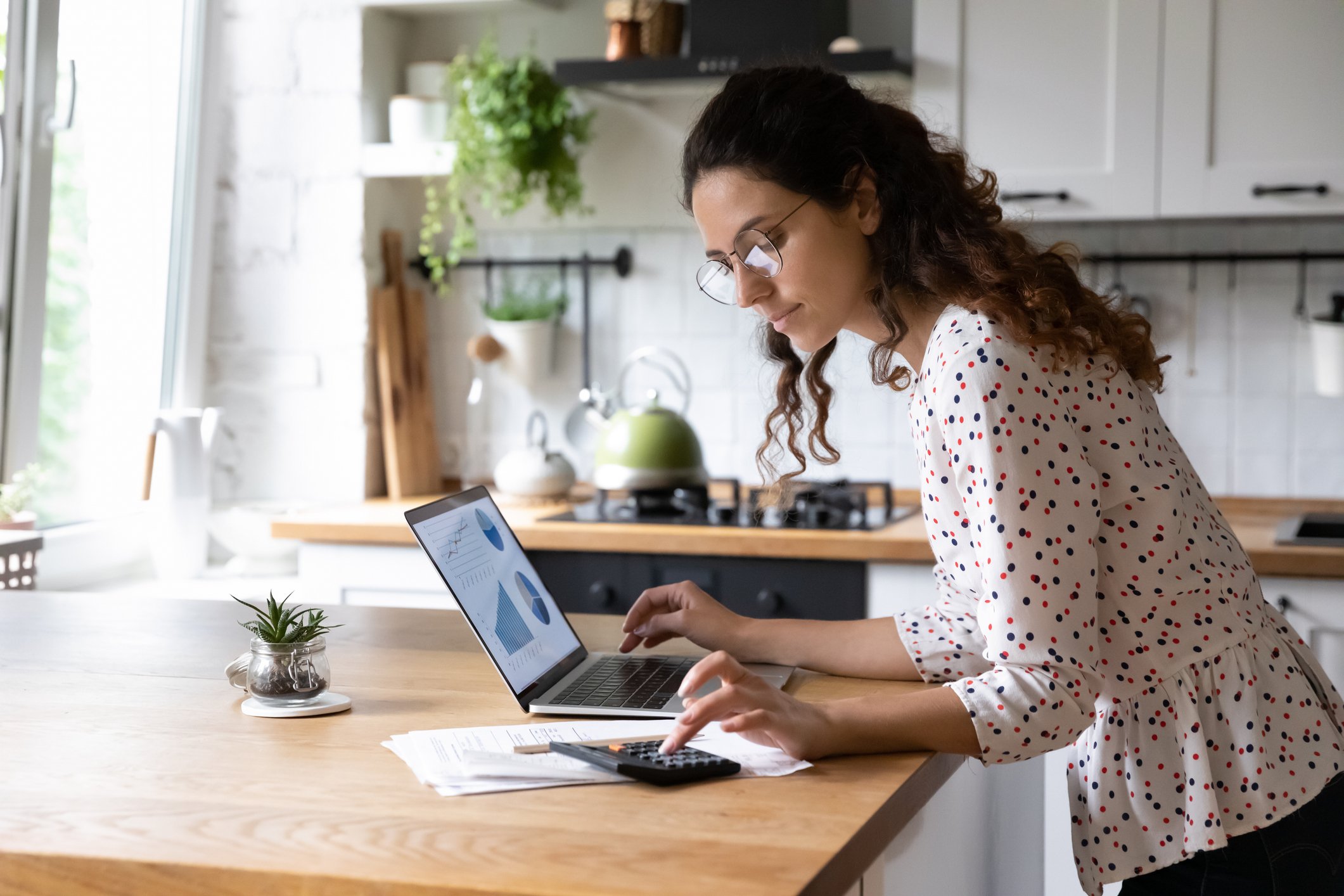 Investor looking at business charts on a laptop in a kitchen.