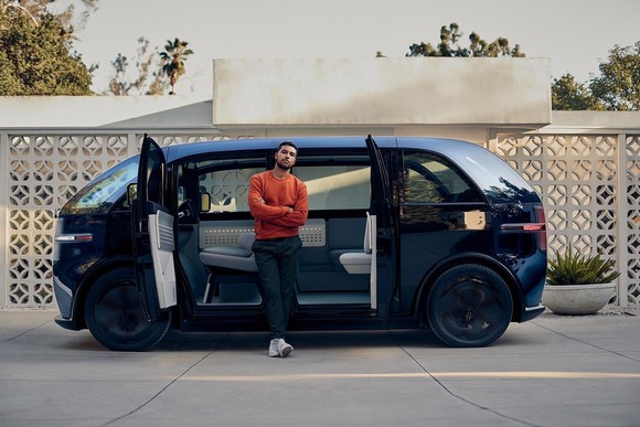 Canoo electric van with owner standing in front of open double doors. 