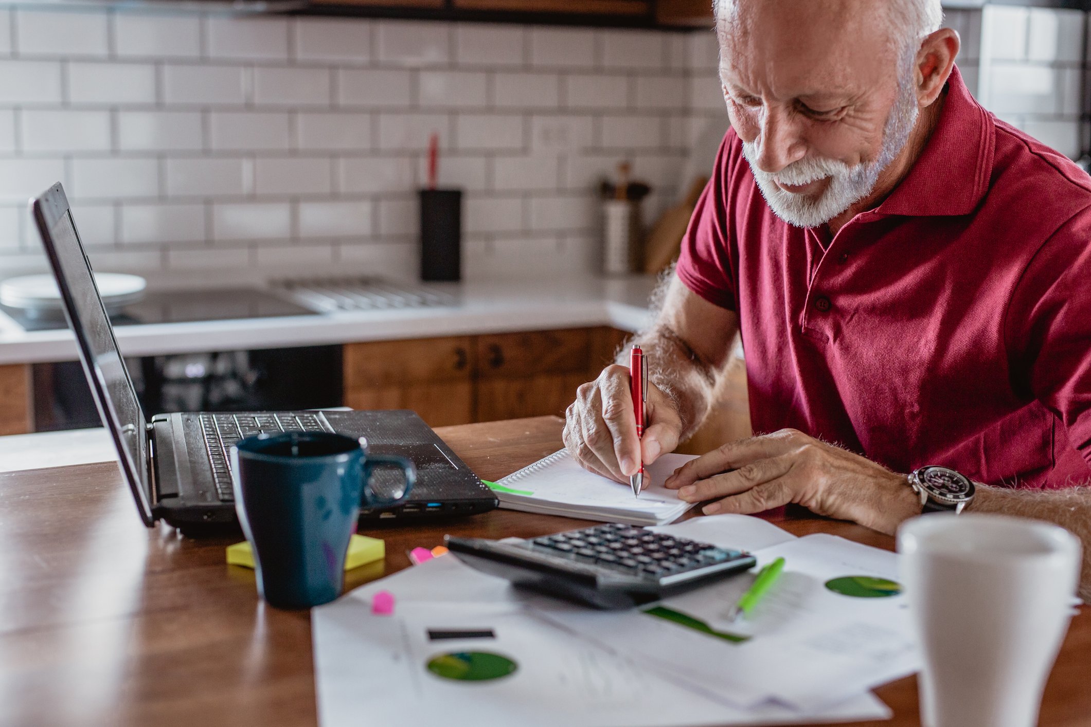 A person writing in a notebook next to a laptop and calculator.