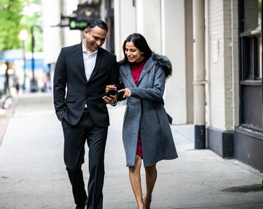 A couple walking and looking at a cell phone.