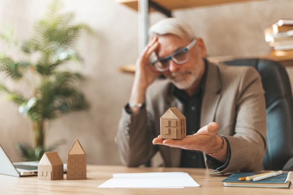 Person holding wooden house block at desk.