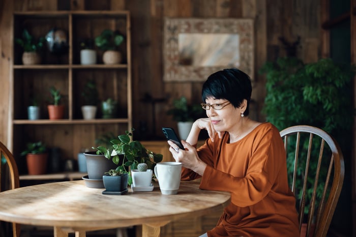Person sitting at dining room table looking at smartphone.