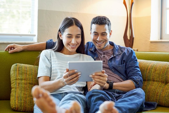 Two people on sofa looking for stocks on a device.