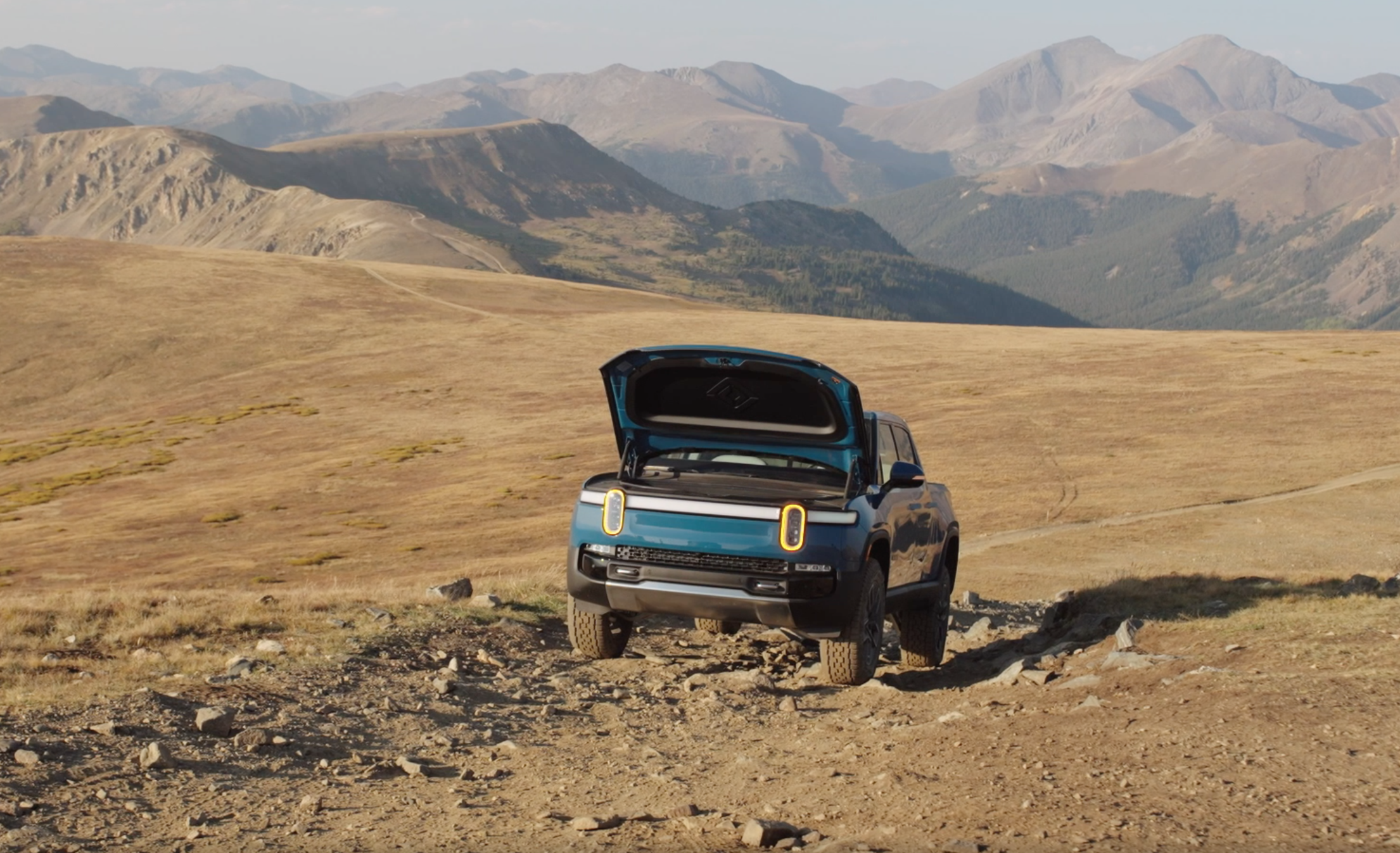 Blue Rivian R1T in field with trunk open. 