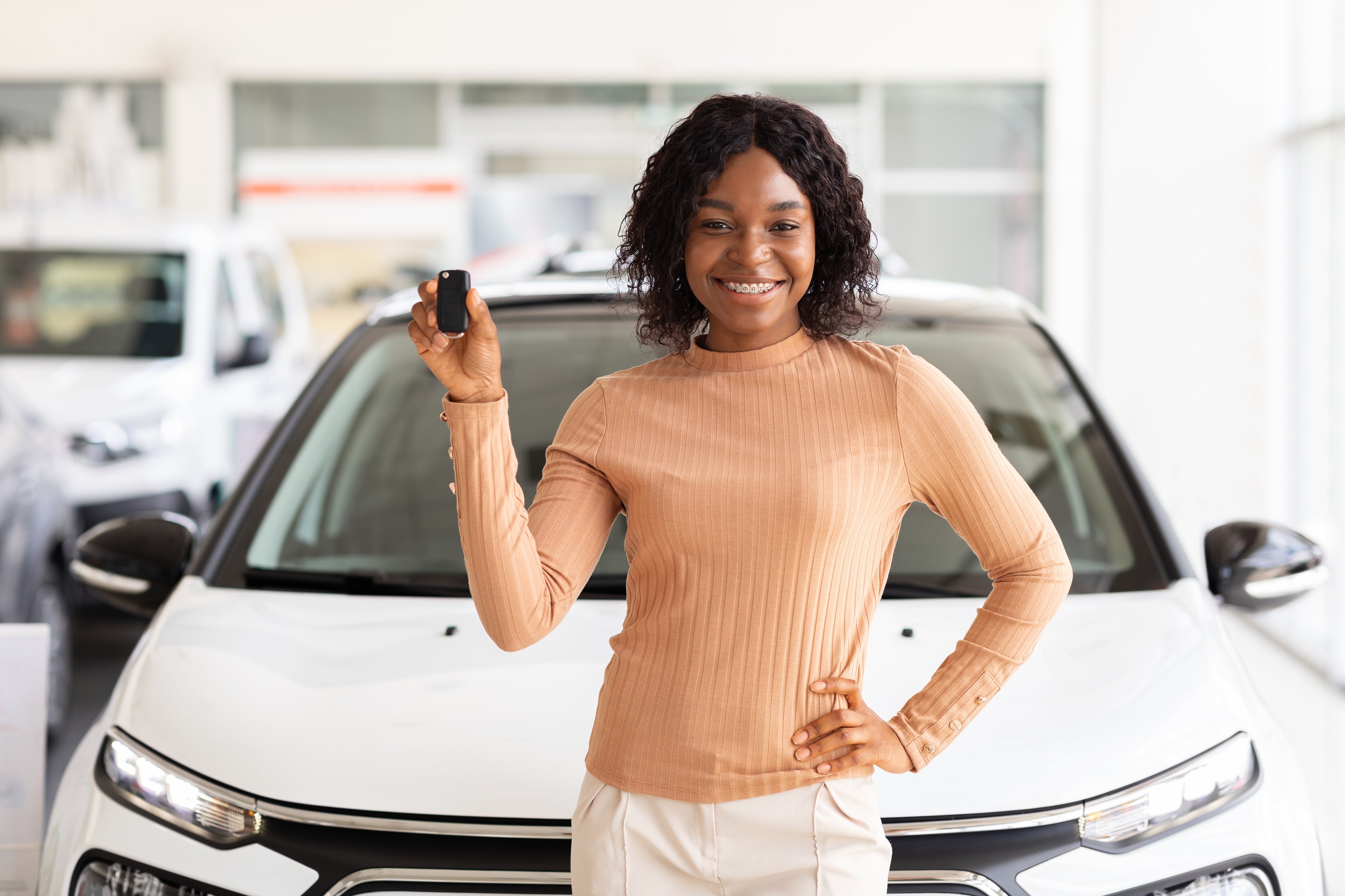 A person holding up keys in front of a car at a dealership.