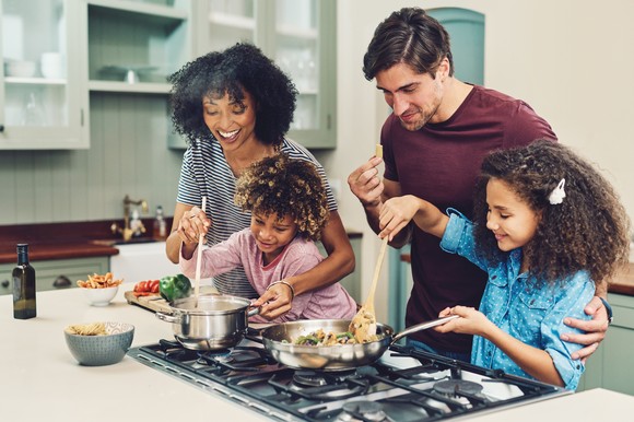 Two parents and two kids cooking a meal together on the stove at home. 