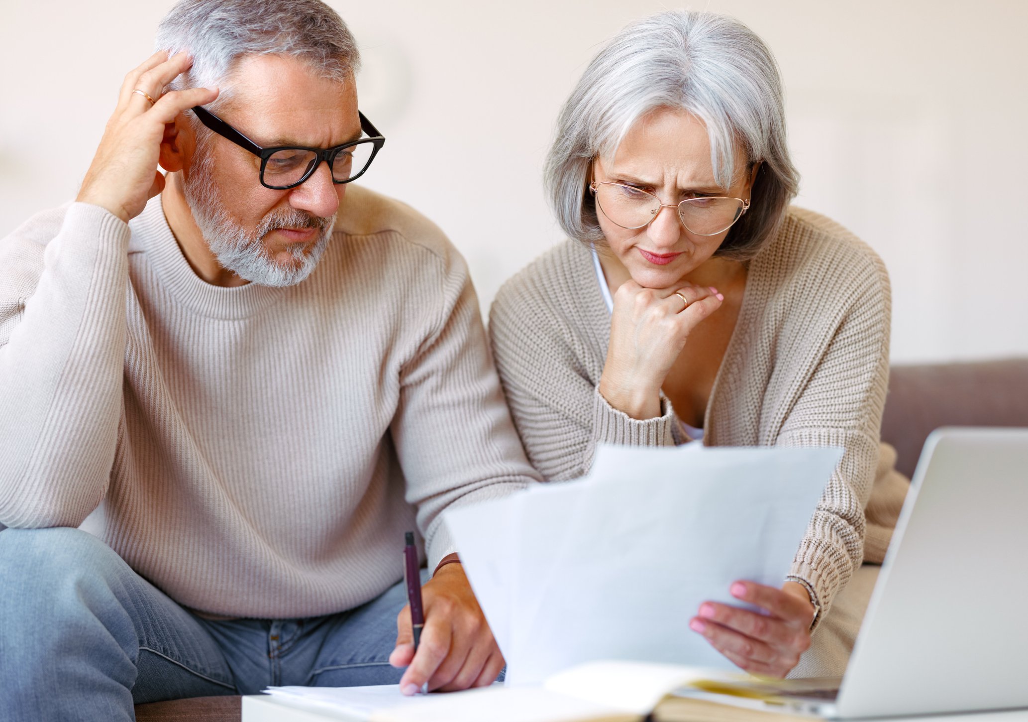 A retired couple sits together on a couch, reviewing financial documents.