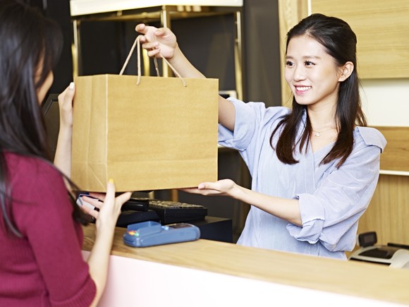 A cashier hands a customer her purchase at a luxury goods store. 