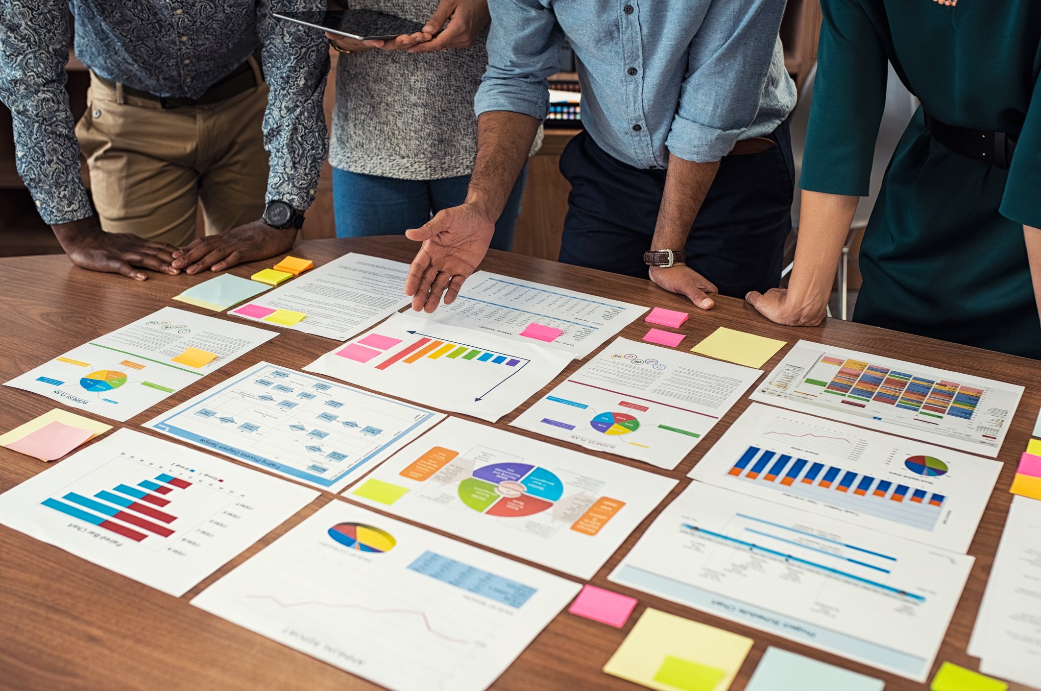 A group of investors stand around a table on which various financial documents and charts are organized.