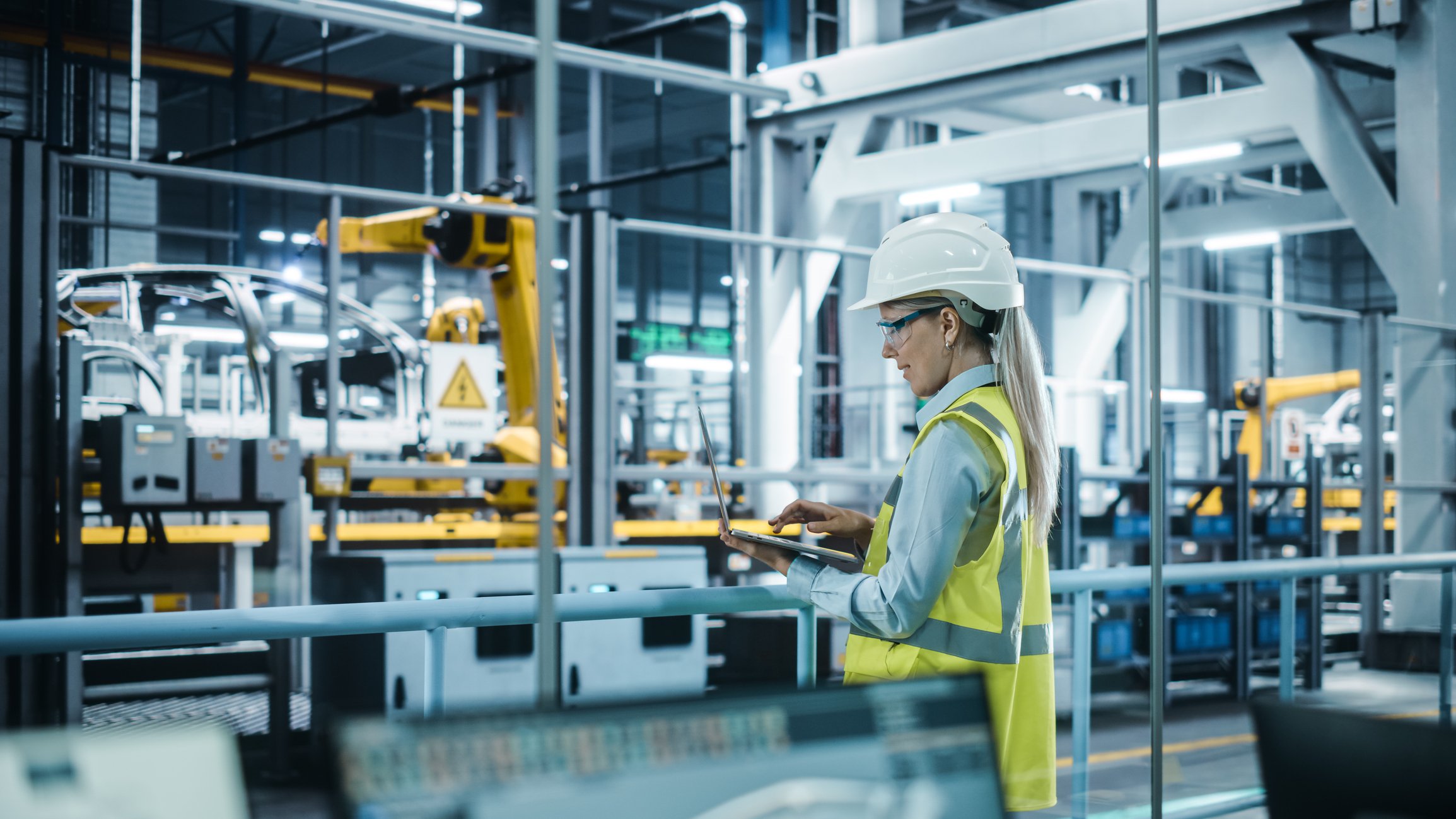 A technician wearing a hard hat interacts with a laptop in an automotive production facility. 