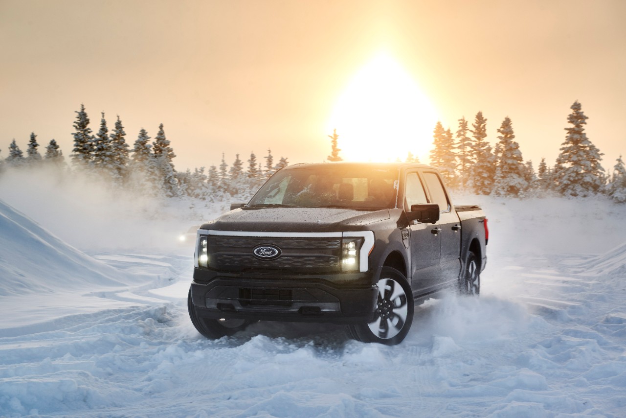 An all-electric Ford F-150 Lightning driving on snowy terrain before sunset.