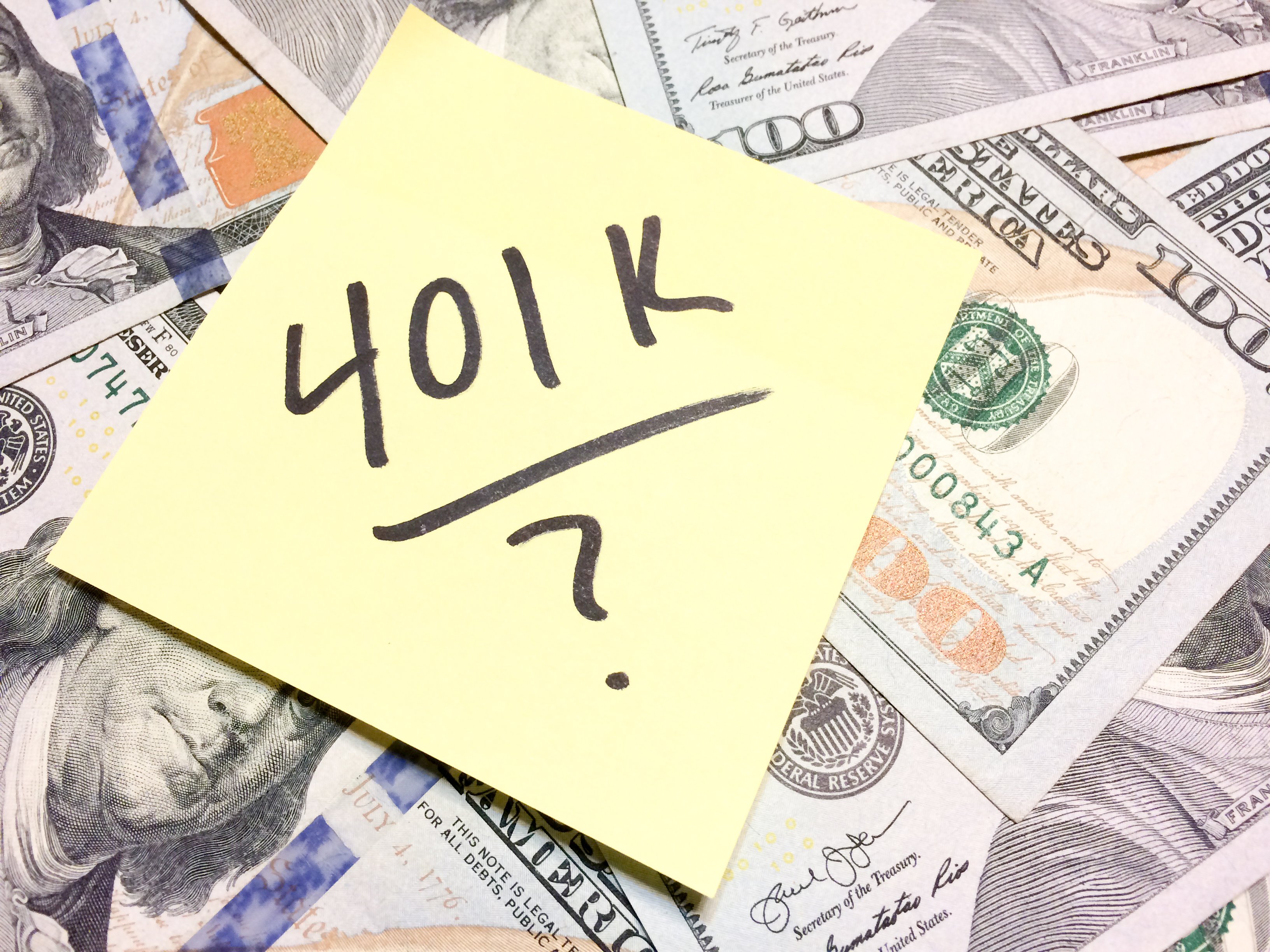 A post-it note reading 401k? laying on a pile of $100 bills.