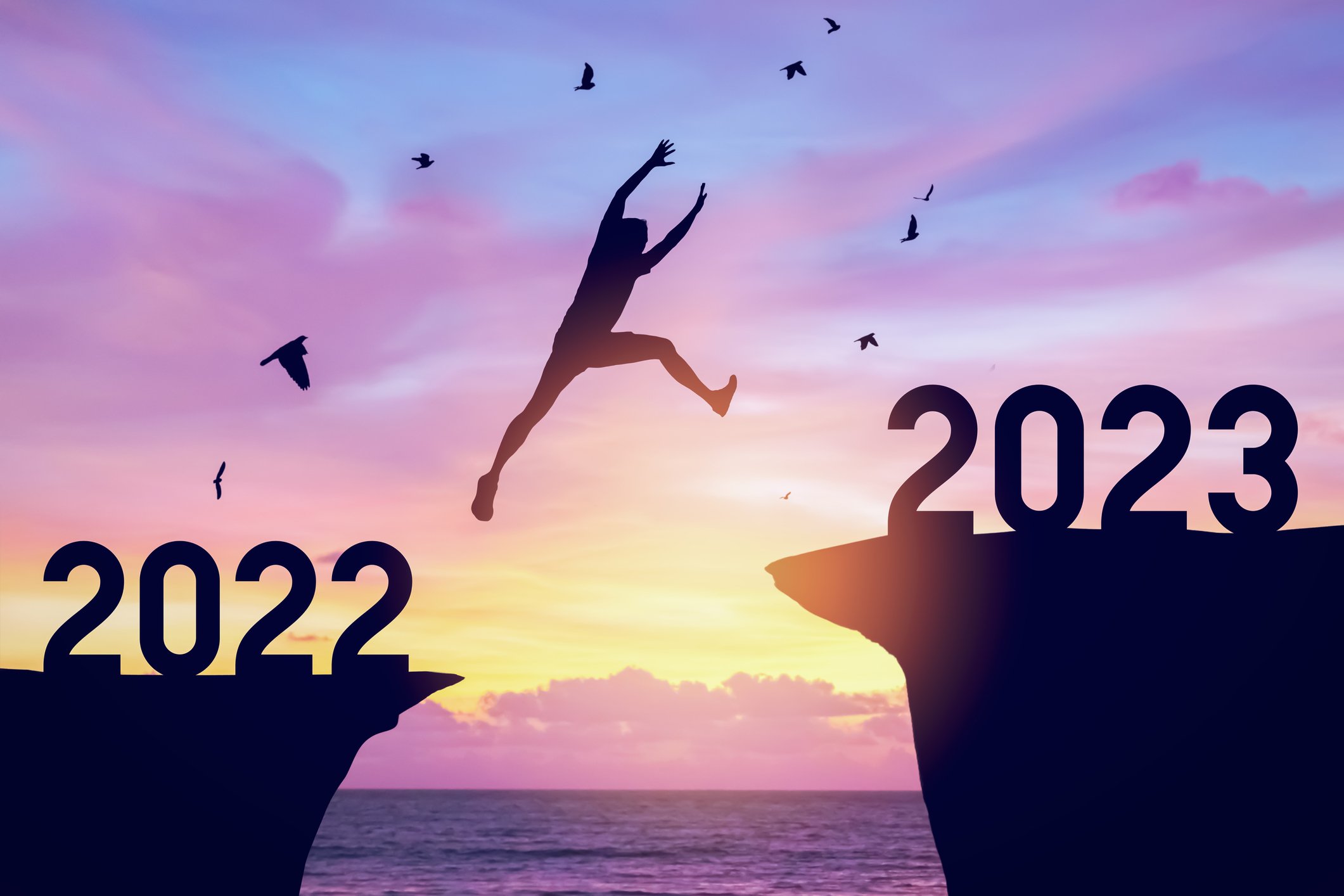 Silhouette of a person leaping from a mountain that says "2022" to a mountain that says "2023" in front of a coastal backdrop. 
