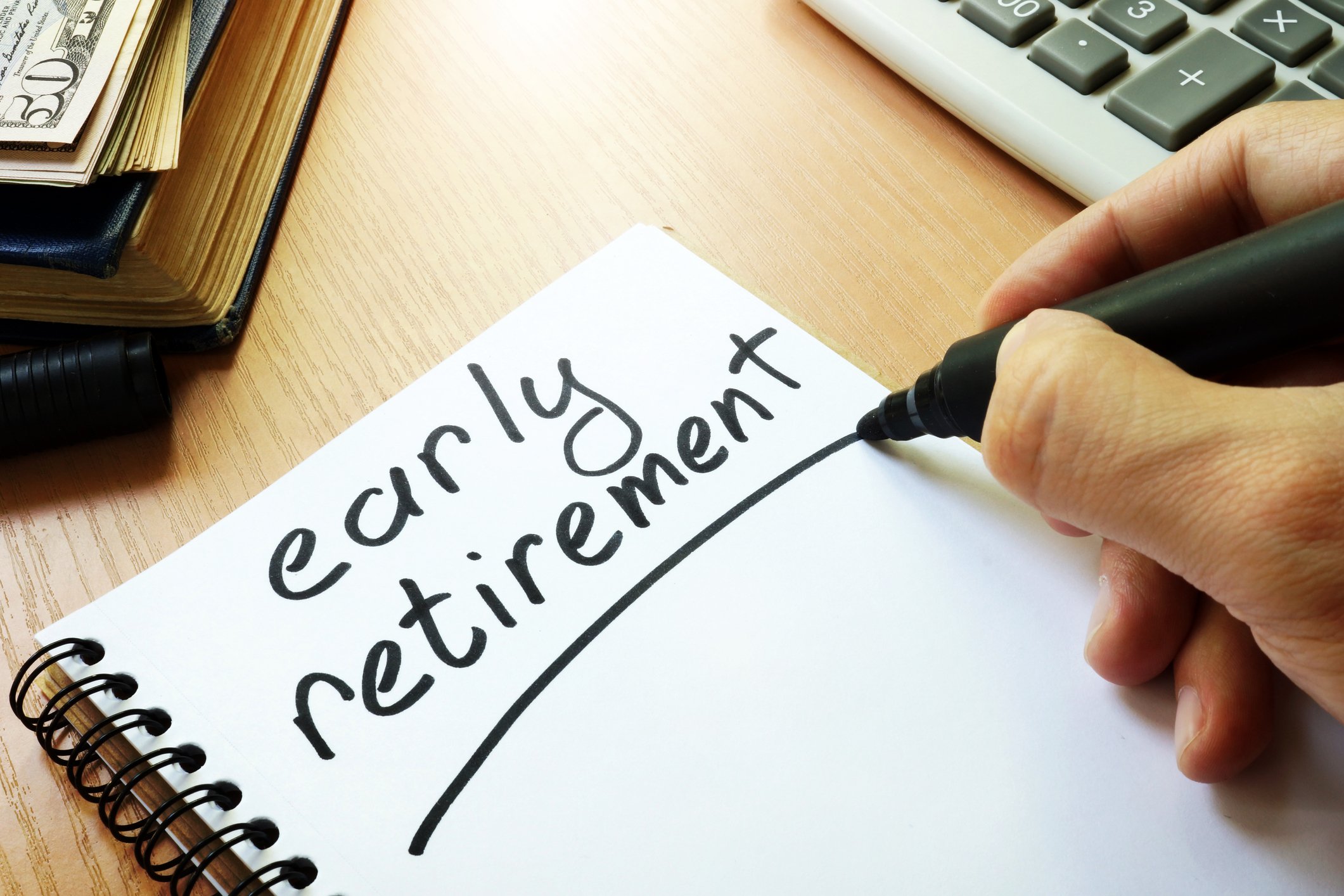 Hand writing the words Early Retirement in a notebook.