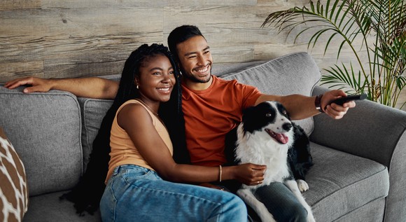 A couple watches TV at home with a dog.