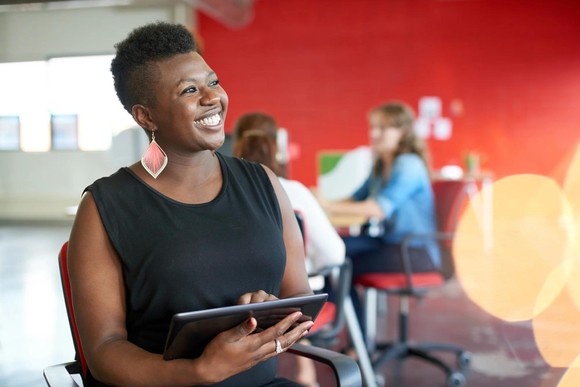 A smiling woman using a tablet at the office. 