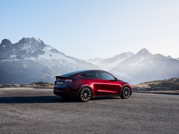 A Tesla Model Y parked in front of a snowy mountain peak.