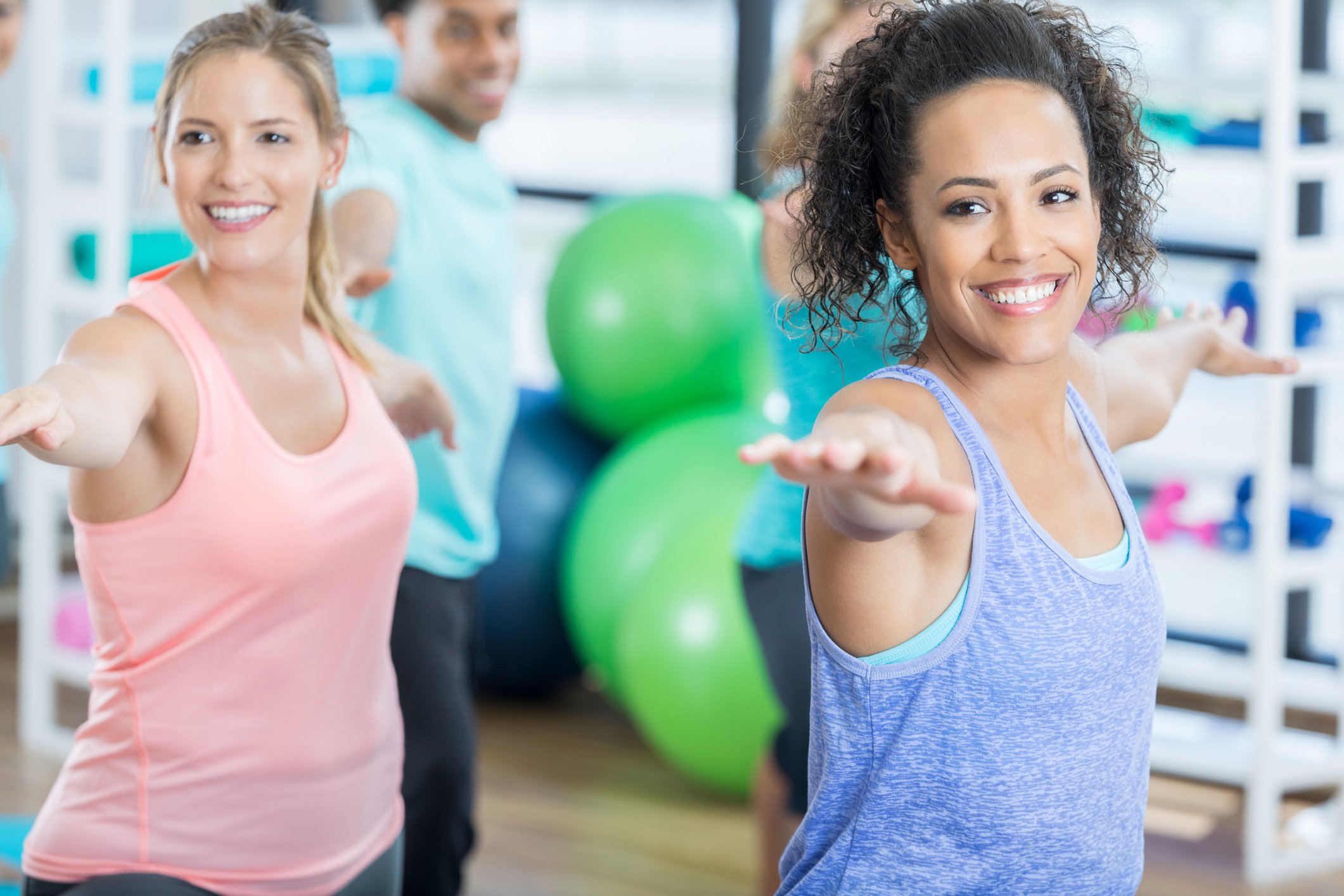 Four adults standing up and stretching their arms during an indoor exercise or yoga class.