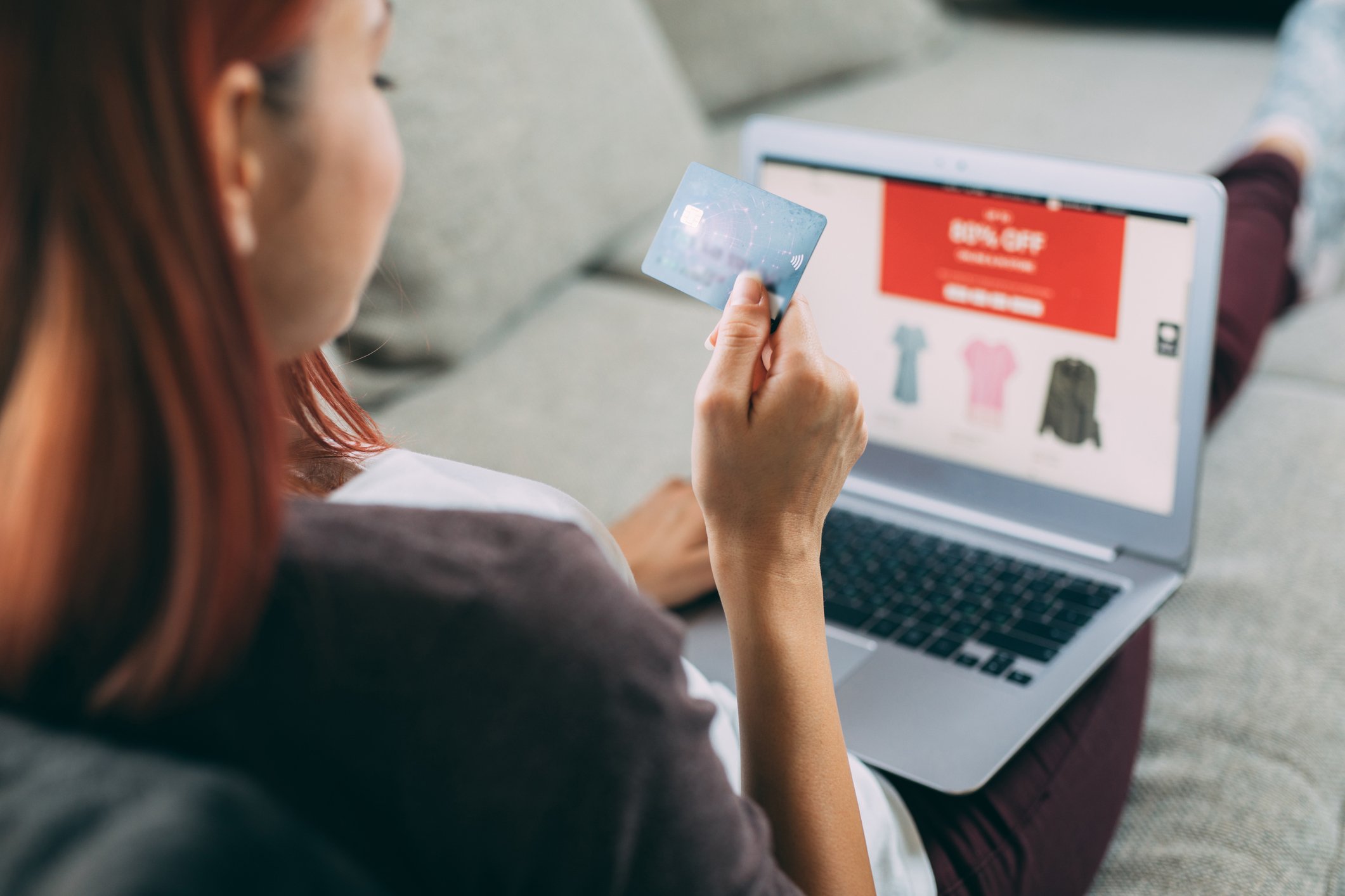 A person holds a credit card while shopping for clothing online.