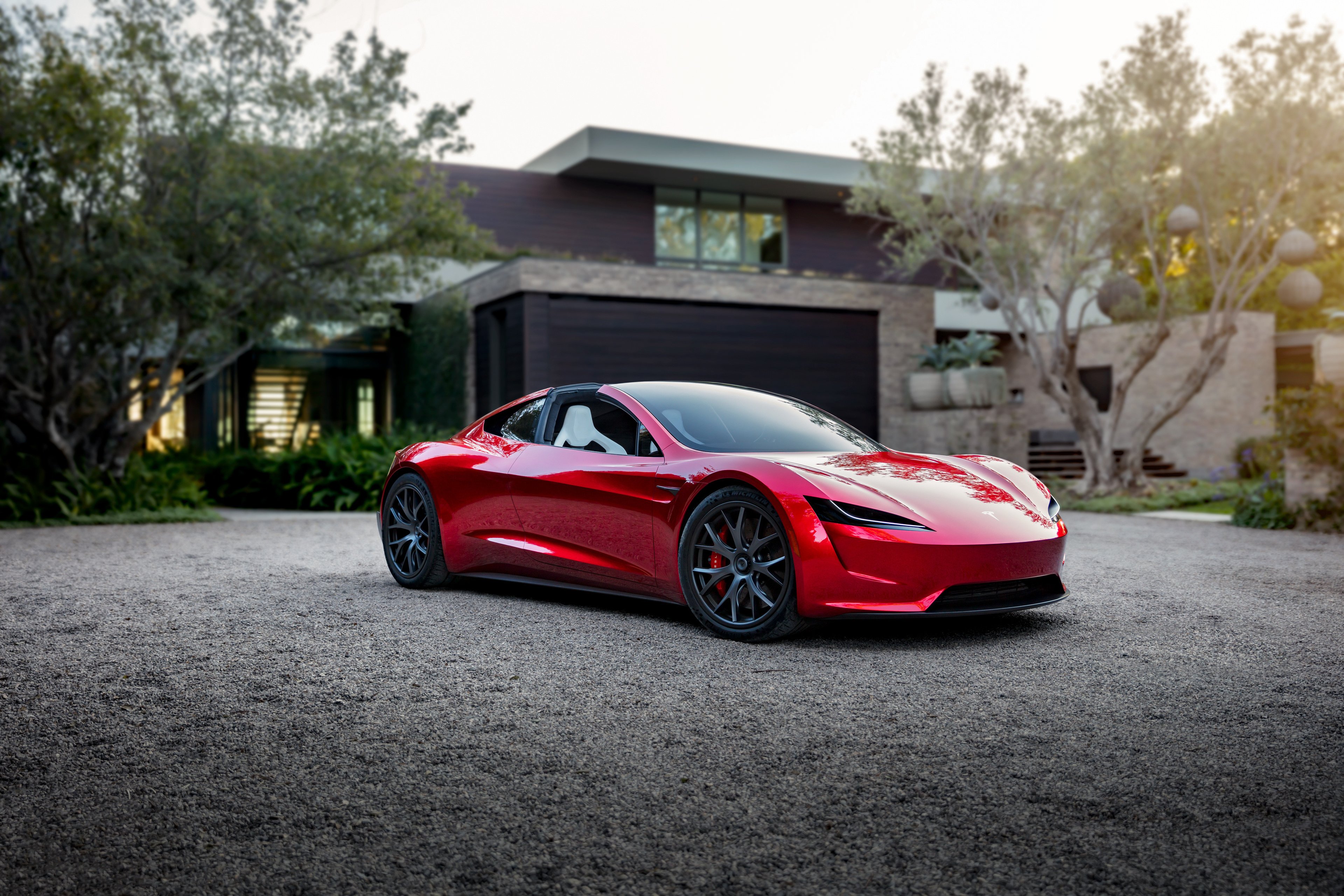 Red Tesla Roadster parked in front of modern home.