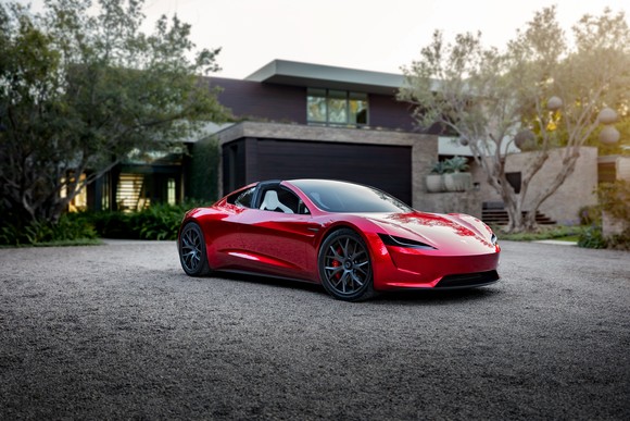 Red Tesla Roadster parked in front of modern home.