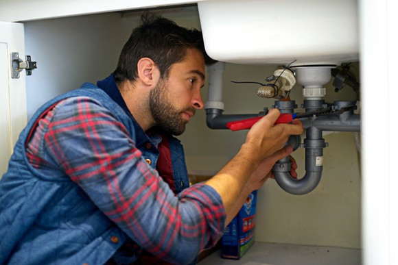 A plumber works on fixing the drain pipe under a sink. 