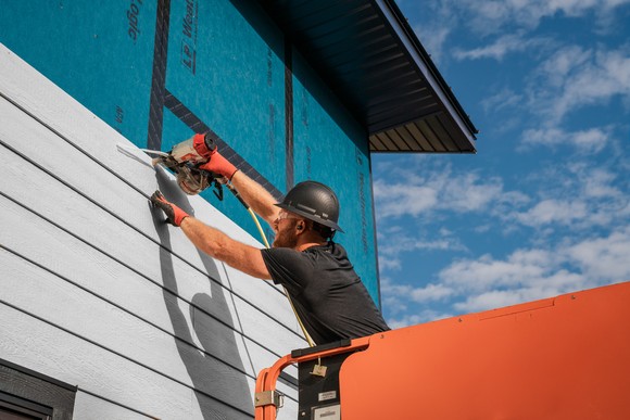 Worker installing siding on a house.