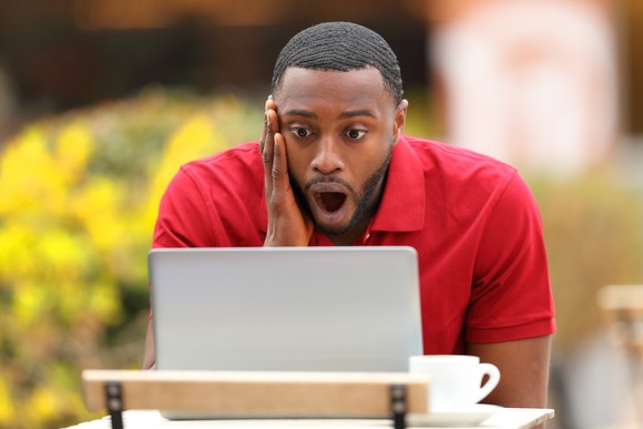 A person with a surprised look on their face looks at a laptop.
