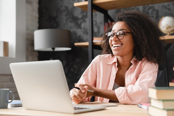 A smiling person works on a laptop computer in a home setting.