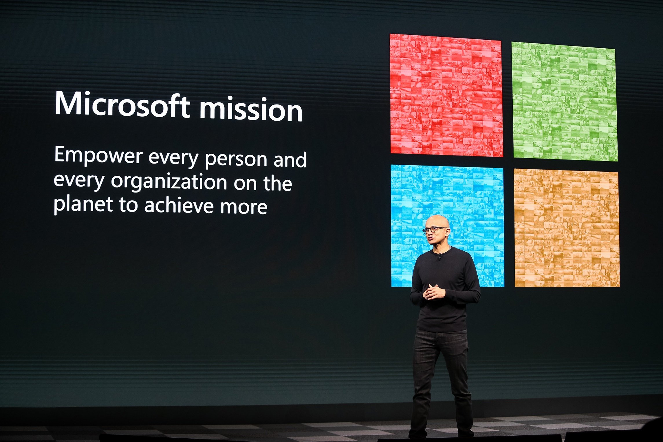 Satya Nadella on stage in front of a screen with Microsoft's logo and mission.