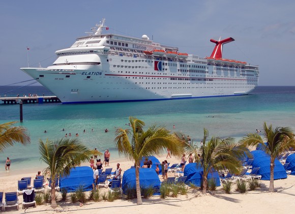 A lively beach scene, with Carnival's ship Elation docked in the background.