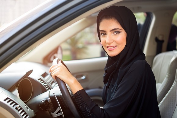 A woman with one hand on the steering wheel of a car.