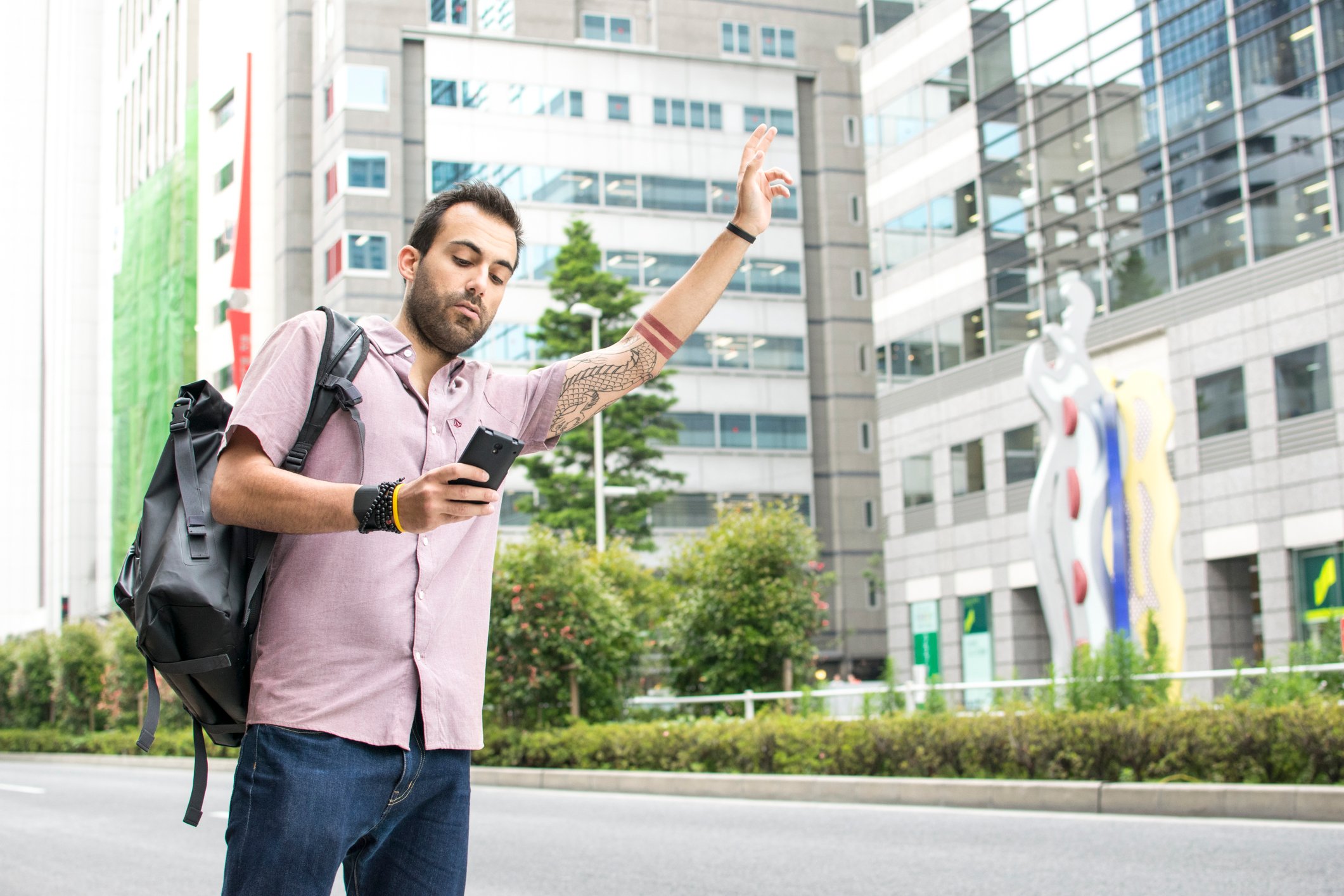 A person standing on the side of a street hailing a ride with a smartphone.