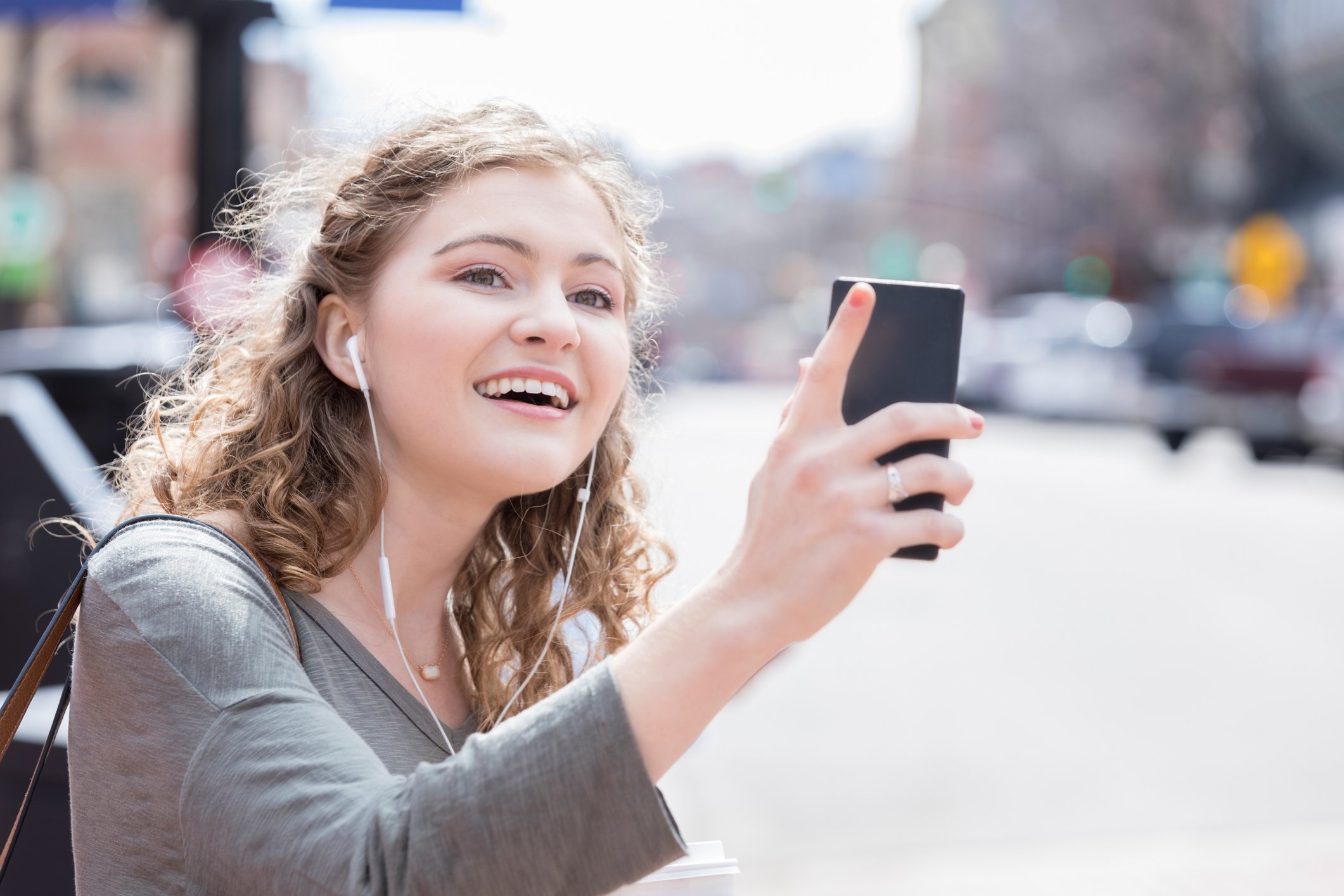 Young woman holds up phone and looks for ride. 