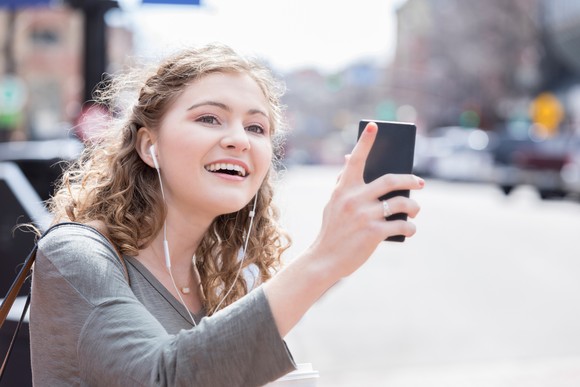 Young woman holds up phone and looks for ride. 