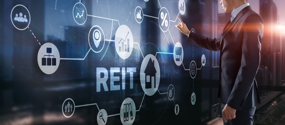A person in a suit pointing at a digital sign that says REIT.