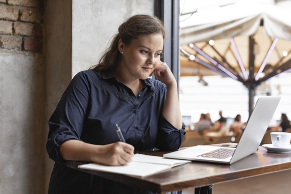 woman taking notes while looking at laptop
