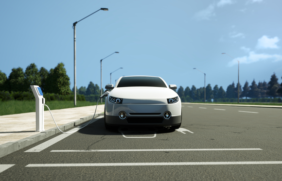 A white electric car charging at a public station in a parking lot.