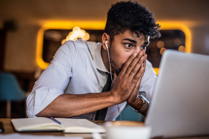 Shocked person with hands over mouth looking at laptop.