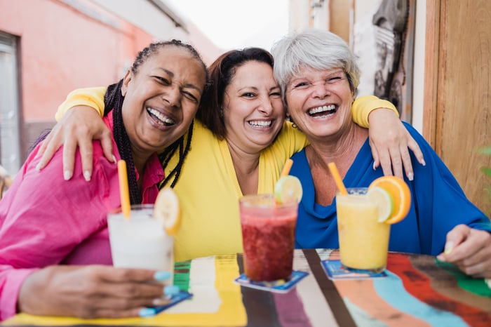 Three friends are smiling, with drinks in front of them.