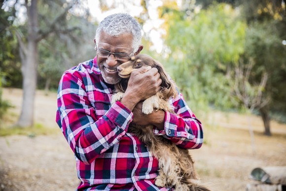 Someone holding and hugging a dog with trees in the background.
