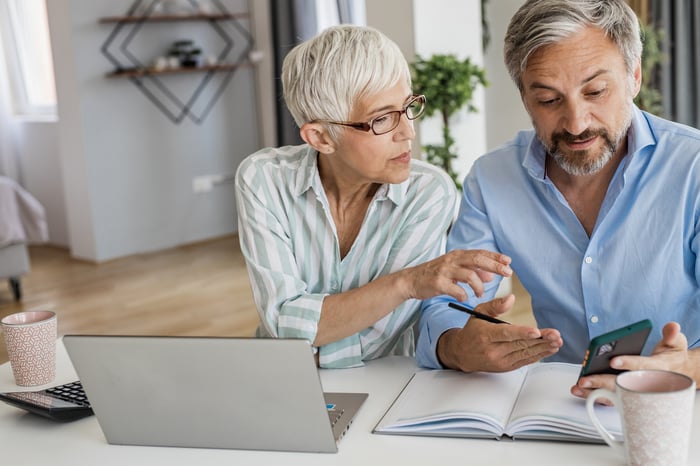 A retired couple is using a calculator while seated at a table.