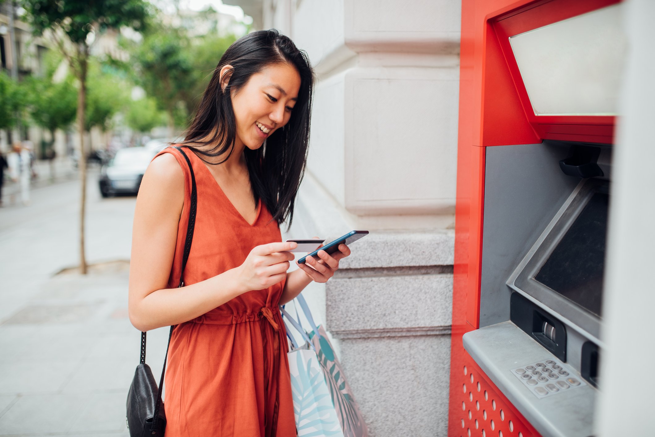 Woman smiles and looks at card near an ATM.