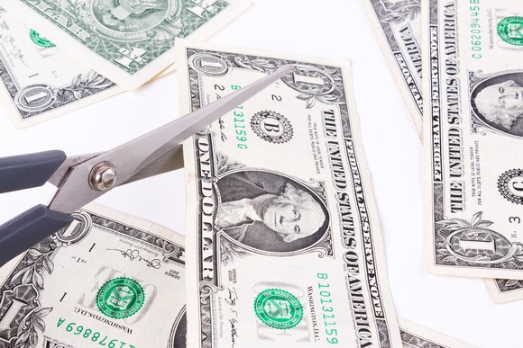 Dollar bill getting cut by scissors.