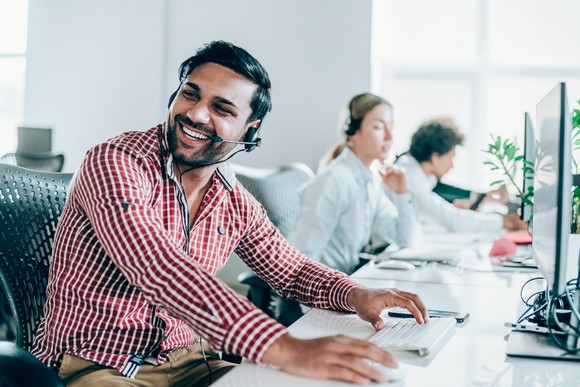 Business sales team in an office, wearing headphones for calling customers and using their computers to record activity.
