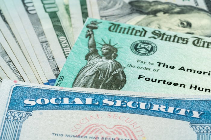 A Social Security card sits atop a U.S. Treasury check and a fan of $100 bills.